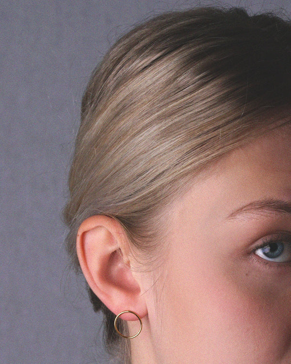A model showcasing the elegance of small gold vermeil Cici circle stud earrings - featuring a delicate circular design, crafted with high-quality sterling silver and 24k gold for a timeless and fashionable look.